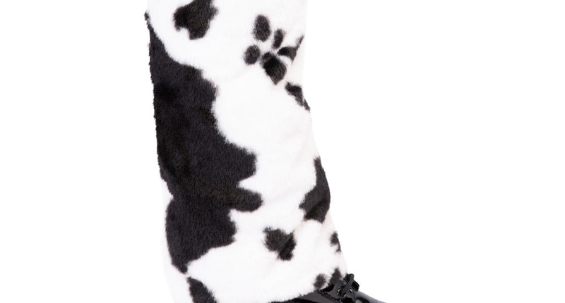 Beenwarmers koe wit met zwarte vlekken over een zwarte schoen, zijaanzicht van de pluizige koker