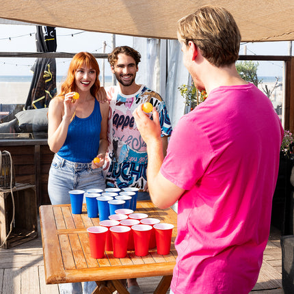 Beer pong drankspel op een houten tafel, drie spelers gooien balletjes naar de bekers