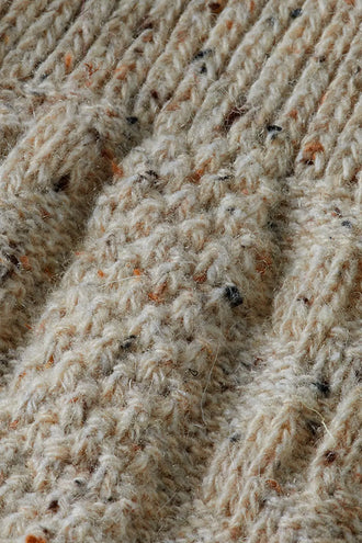 Detail van het gemêleerde beige garen met oranje en zwarte spikkels in de kabelsteek