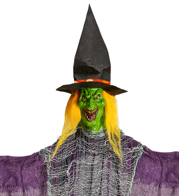 Detail van het groene heksengezicht met grijns, geel haar en zwarte punthoed met oranje band