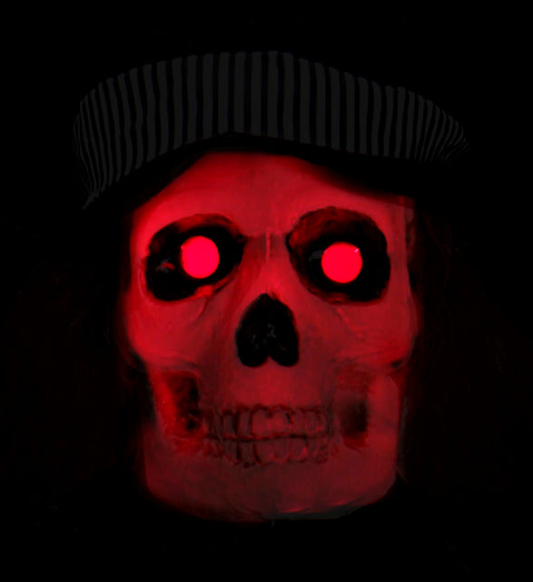 Detail van de skeletkop met rood oplichtende ogen en gestreepte hoedband