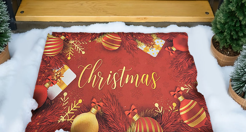 Deurmat 'Christmas' in rood met gouden letters en kerstballen, in de sneeuw voor de voordeur tijdens Kerst