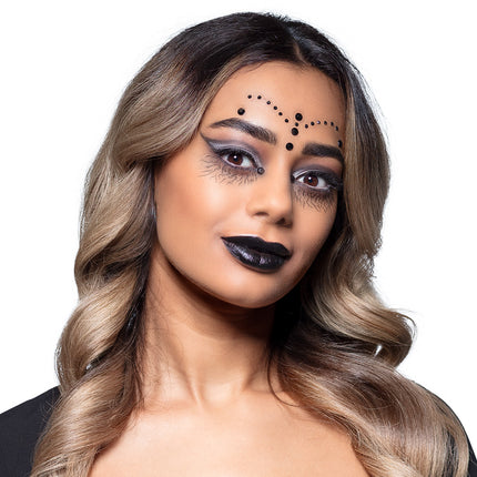 Gothic witch look met zwarte gezichtssteentjes op het voorhoofd en diepzwarte lippen voor Halloween