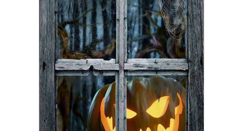 Griezelige raamdeco met oplichtende pompoenkop en spinnenwebben achter een verweerd grijs kozijn voor Halloween