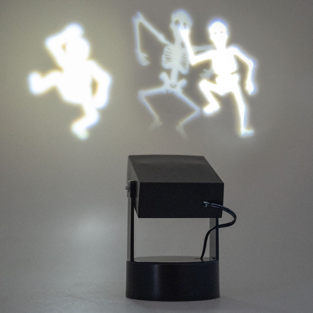 Halloween projector met dansende skeletten in werking, drie witte skeletsilhouetten op de wand tijdens Halloween