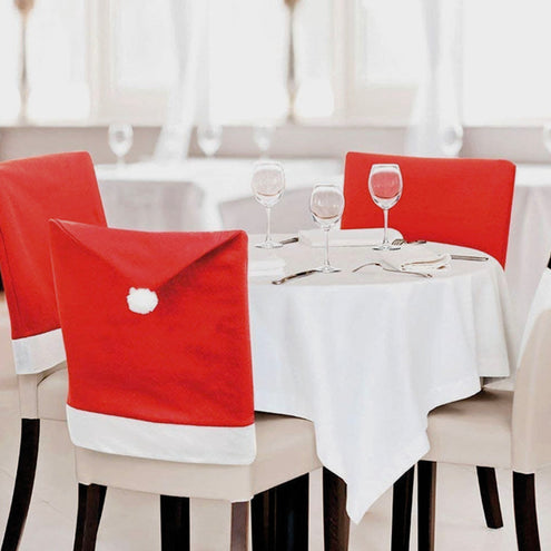 Kerstmuts stoelhoezen met witte pompon aan een gedekte kersttafel met wijnglazen