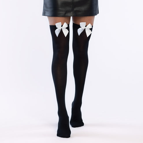 Kniekousen zwart met witte strik gedragen boven de knie bij een korte zwarte rok, dames beenmode