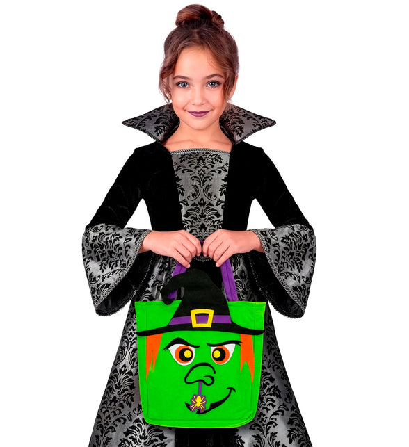 Meisje draagt de groene heksen snoeptas aan de paarse hengsels tijdens Halloween