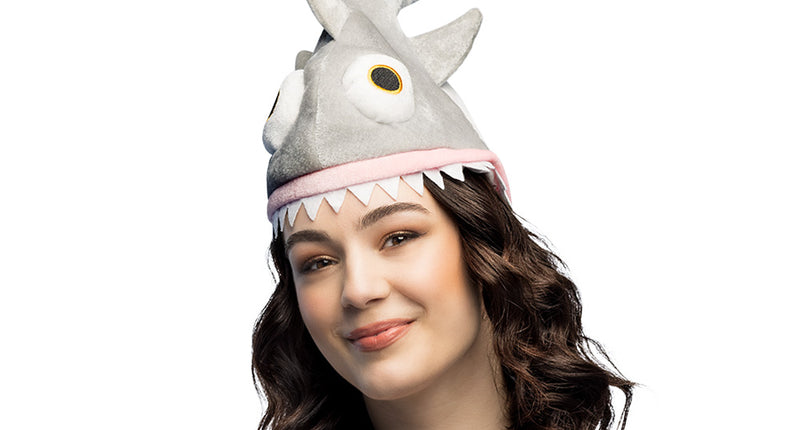Muts haai in grijs plush met opstaande staartvin en witte tandenrij, gedragen door een dame op een themafeest