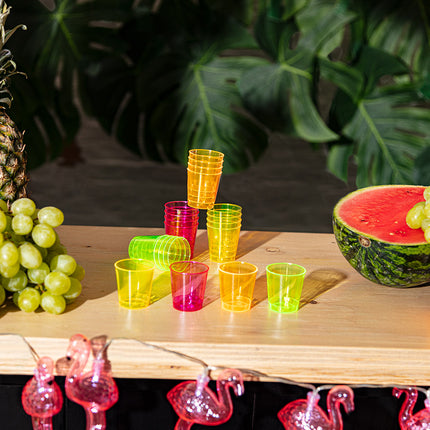 Neon shotglaasjes op een houten bar met tropisch fruit en flamingoverlichting