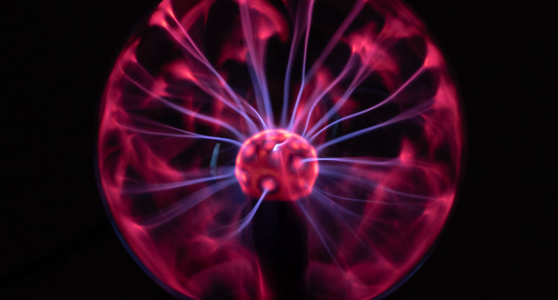 Plasmalamp met roze en violette lichtbogen in de glazen bol, oplichtend in het donker