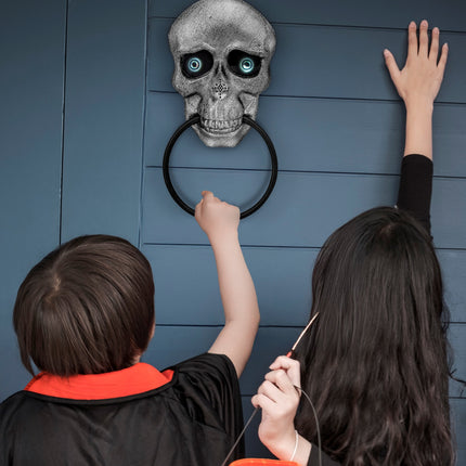 Schedel deurklopper aan blauwe voordeur terwijl kinderen op halloweenavond aan de ring trekken