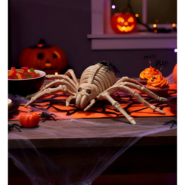Spinnen skelet op een halloweentafel met spinrag, pompoenen en cupcakes